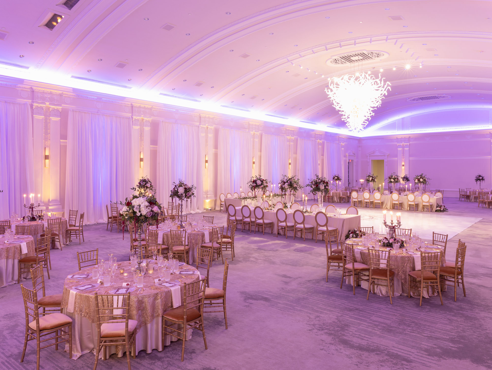 Elegant Royal Glam Gatsby Wedding Reception Decor, Purple Uplighting, White Ballroom Dance Floor with Custom Gold Monogram, Long Table with Champagne Linen, Gold and Ivory Dining Chairs, Tall Glass Vases with Lush Greenery, White, Mauve, Burgundy and Blush Pink Roses with Red Hanging Amaranthus Flower Centerpieces | Tampa Bay Wedding Planner and Designer John Campbell Weddings | St. Pete Wedding Rentals Kate Ryan Event Rentals