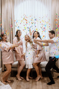 Bride with Bridesman and Bridesmaids Wearing Matching Pink Robes Popping Colorful Confetti | Tampa Bay Wedding Hair and Makeup Femme Akoi Beauty Studio