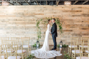 Winter Modern Whimsical Wedding Styled Shoot Ceremony Decor, Bride Wearing Sleek Long Sleeve Lace and Illusion Wedding Dress and Groom Kissing, Copper Rectangular Arch with Greenery Leaves, Black Lanterns, Gold Chiavari Chairs | Tampa Bay Wedding Planner MDP Events Planning | Madeira Beach Industrial Wedding Venue The West Events | Wedding Dress Truly Forever Bridal Tampa