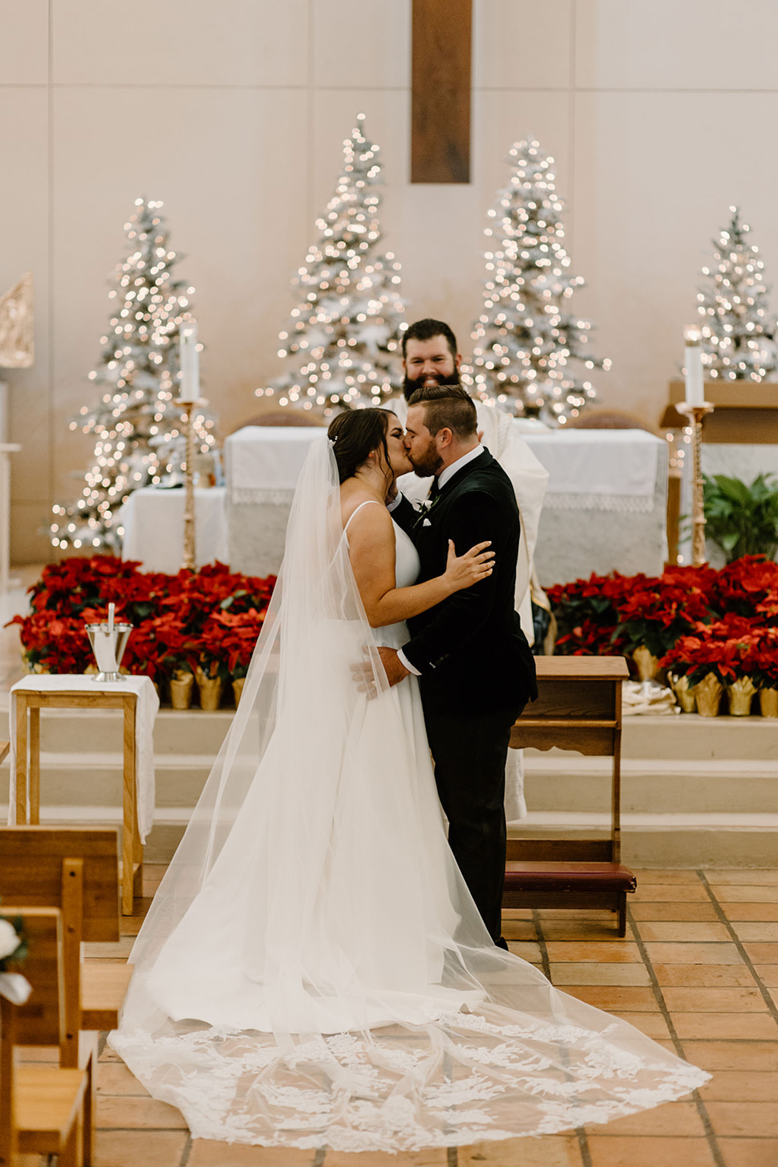 Bride and Groom at the Alter in Christmas Church Wedding Ceremony with Red Floral Accents First Kiss Portrait | Tampa Wedding Florist FH Events