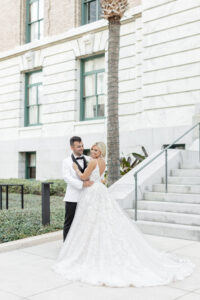 Modern Romantic Bride Wearing Floral Lace and Tulle Open V Back Ballgown Wedding Dress with Groom in White and Black Collar Tuxedo