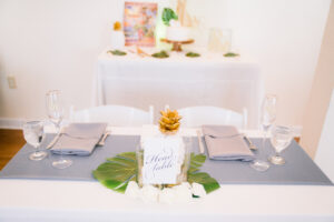 White Chairs and White Linen Table with Gray Napkins and Runner | Monstera Leaf and Tropical Wedding Reception Tablescape