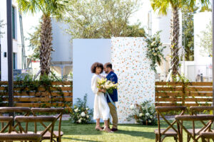 Modern Whimsical Wedding Ceremony Decor, Light Blue and Terrazzo Panel Backdrops, Bride Wearing Casual Flowy Mid Length Wedding Dress and Groom in Blue Suit Jacket with Khaki Pants, Wooden Cross Back Chairs | Tampa Bay Wedding Venue Florida Ave Brewing