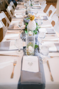 White Chairs and White Linen Table with Gray Napkins and Runner | Monstera Leaf and Tropical Wedding Reception Tablescape