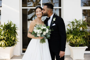 Classic and Timeless Bride Holding White Roses and Greenery Leaves Floral Bouquet and Groom Outdoor First Look Wedding Portrait | Wedding Venue Tampa Garden Club | Wedding Hair and Makeup Femme Akoi Beauty Studio | Wedding Florist Monarch Events and Designs