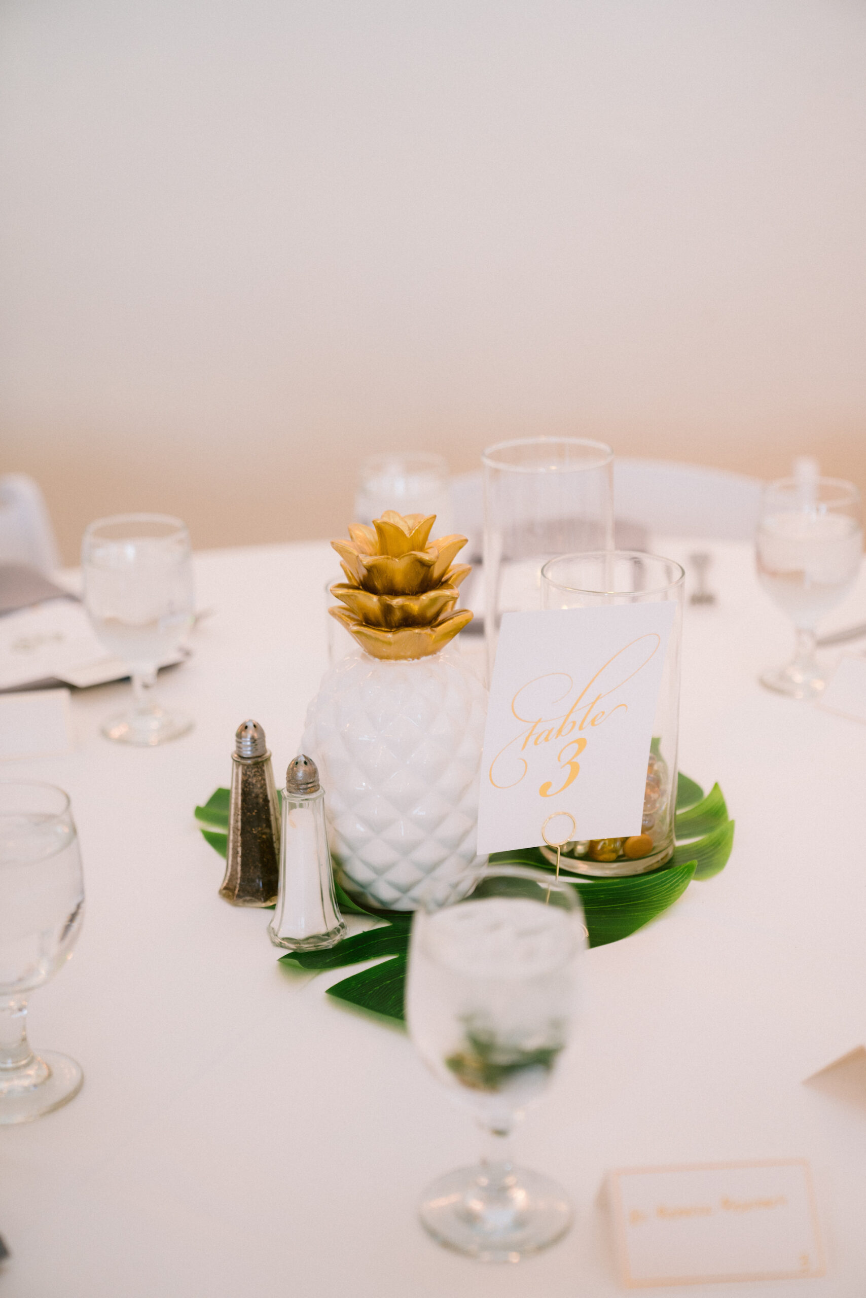 White Chairs and White Linen Table with Gray Napkins and Runner | Monstera Leaf and Tropical Pineapple Centerpiece