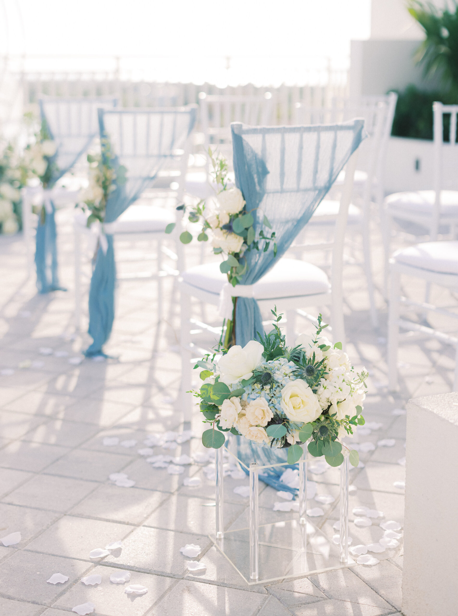 White Ceremony Chairs with Blue Draping and White Floral and Greenery Detailing | Tampa Wedding Rentals Gabro Event Services