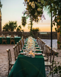 Green Emerald Linens on Long Feasting Reception Tables Romantic Candle Centerpieces Hanging Floral Arrangements | Outdoor Beach Decor Ideas