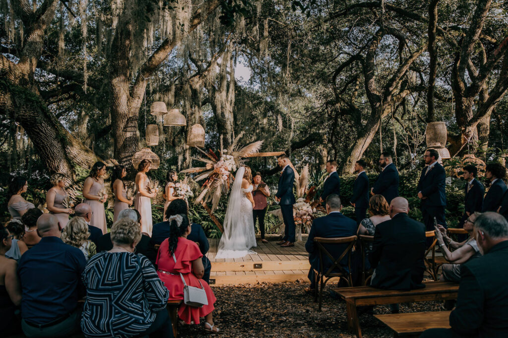 Bride and Groom Exchanging Wedding Vows, Boho Vintage Wedding Ceremony Decor, Lush Neutral Pampas Grass, Blush Pink and White Roses, Dried Palm Leaves, Terracotta Flower Arrangement on Geometric Hexagon Wooden Arch, Hanging Wicker, Rattan Lamp Shades on Trees | Tampa Bay Wedding Planner Stephany Perry Events | Wedding Venue Mill Pond Estate