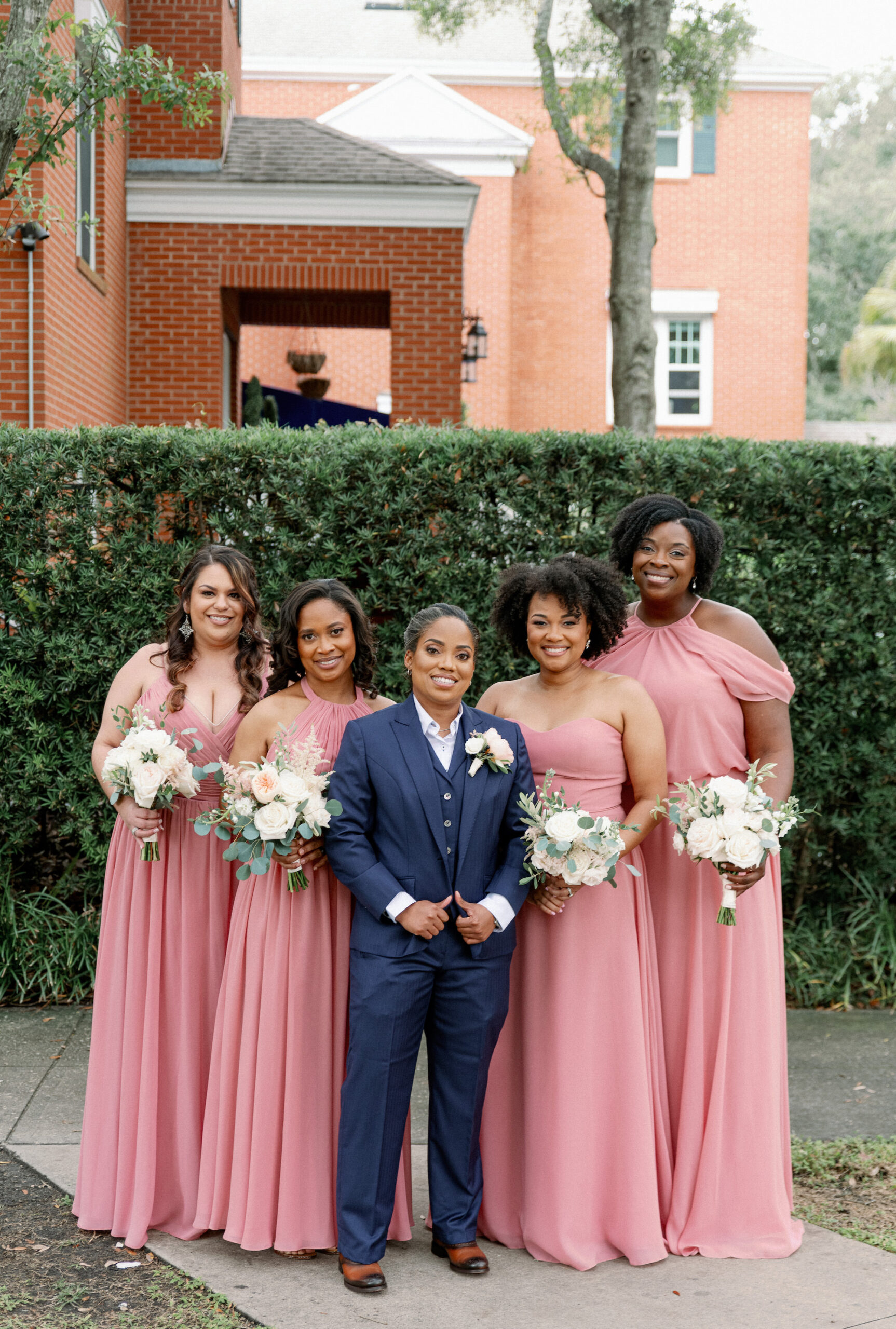 Same Sex Lesbian Wedding, Bride Wearing Blue Suit with Bridesmaids in Mix and Match Pink Dresses Holding Lush White and Greenery Floral Bouquets | Tampa Bay Wedding Photographer Dewitt for Love Photography | Wedding Hair and Makeup Imago Dei by Milan