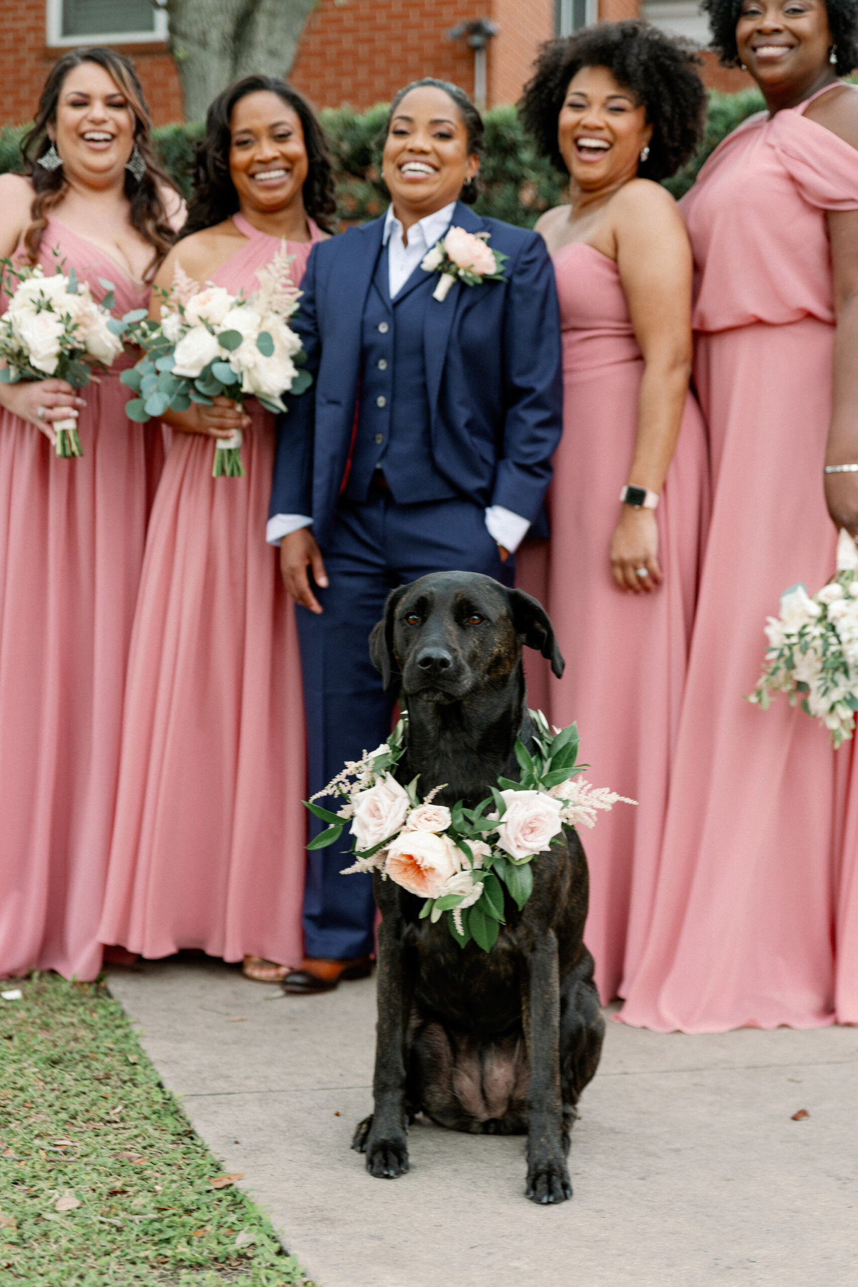 Same Sex Lesbian Wedding, Bride Wearing Blue Suit with Bridesmaids in Mix and Match Pink Dresses Holding Lush White and Greenery Floral Bouquets with Dog in Floral Collar | Tampa Bay Wedding Photographer Dewitt for Love Photography | Wedding Hair and Makeup Imago Dei by Milan