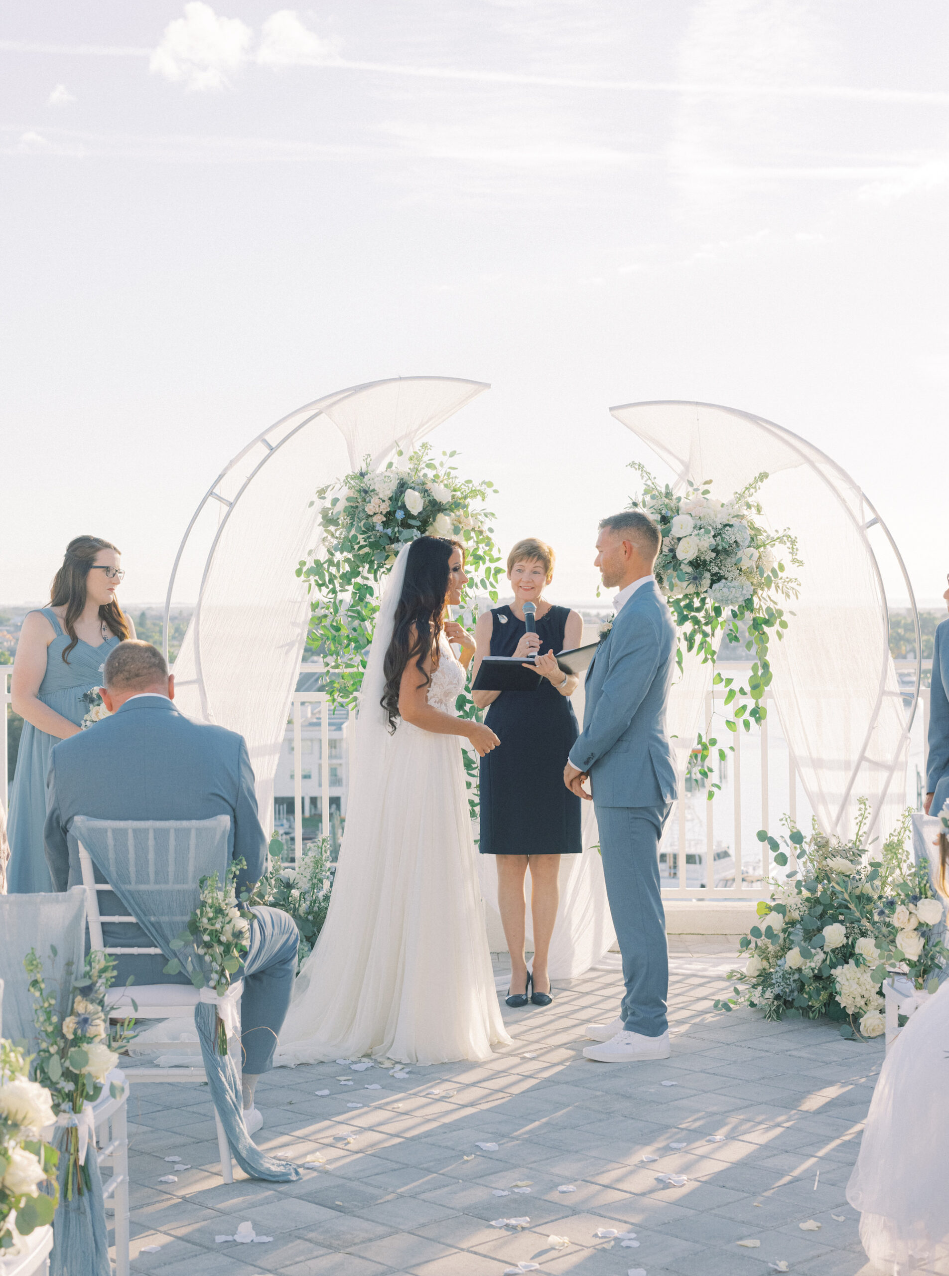 Bride and Groom Exchange Vows | Outdoor Romantic Wedding Ceremony with White Chairs | Two Half Circle Arch with White Floral and Greenery Details | Tampa Wedding Officiant A Wedding with Grace