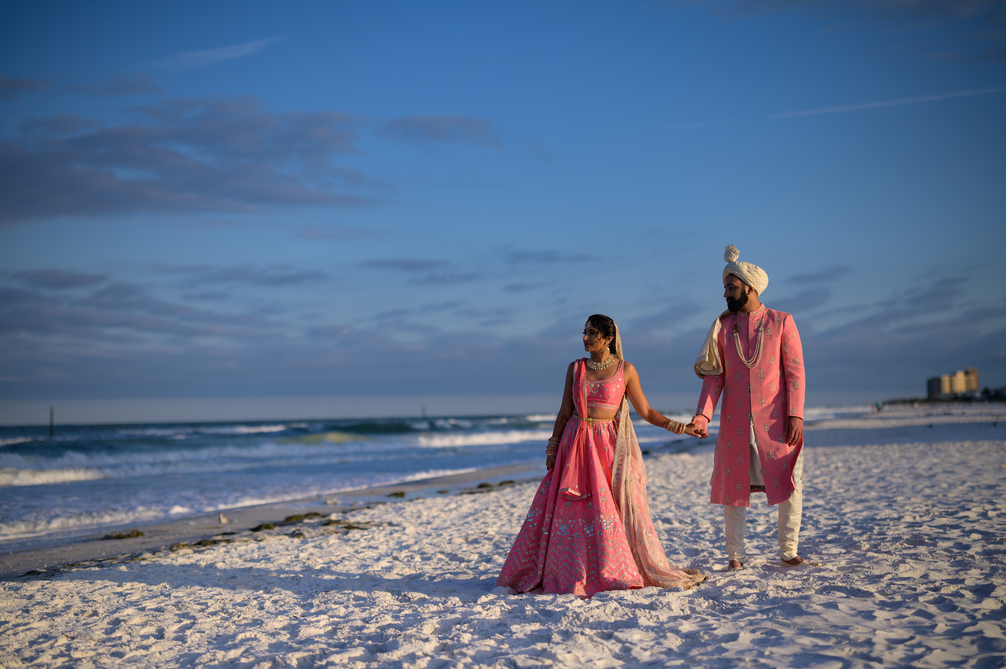 Bride and Groom Walk Down Beach, Wearing Traditional Indian Wedding Attire in Bright Pink and Gold | Florida Wedding Venue Hilton Clearwater Beach Resort