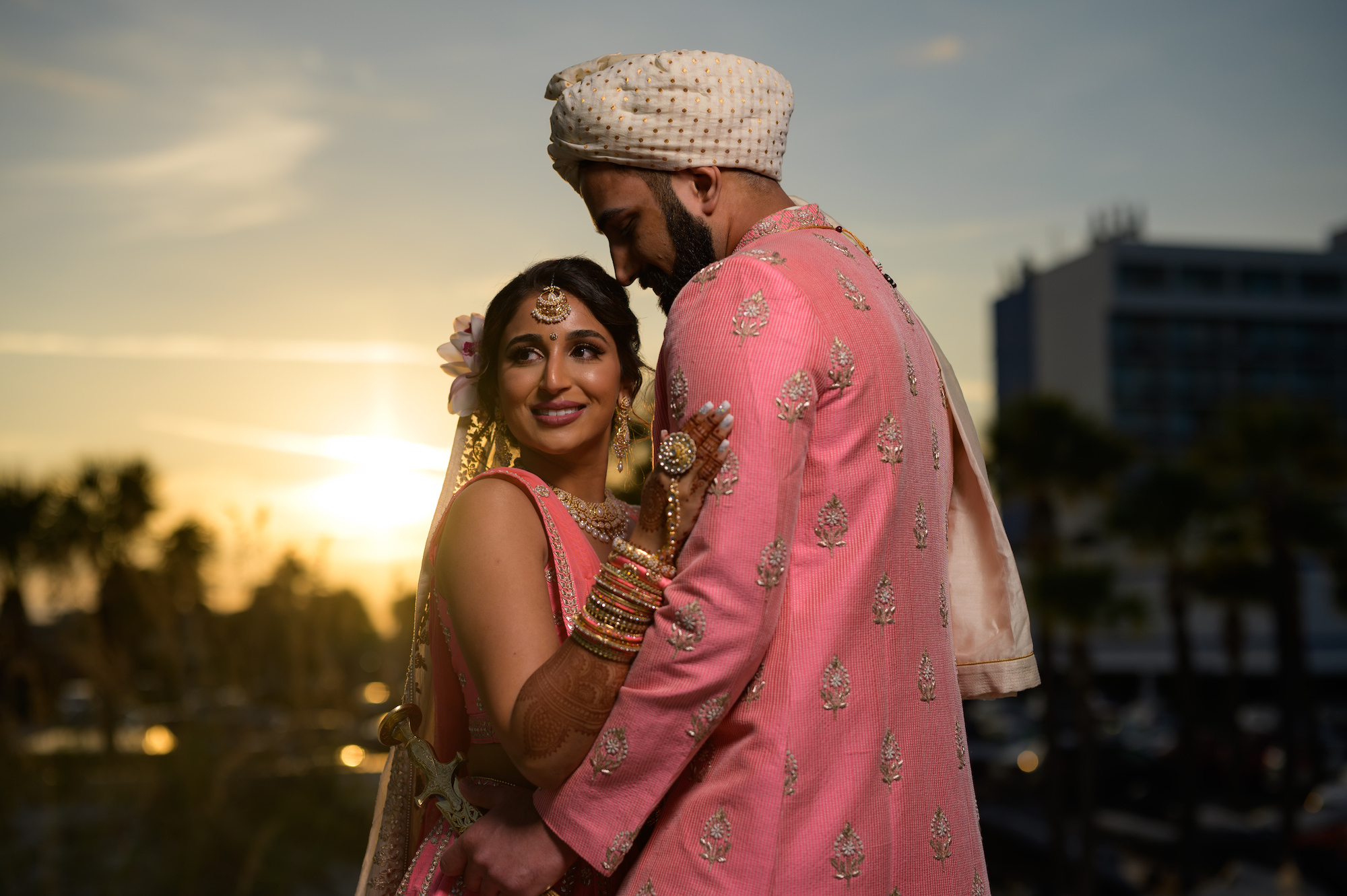 Bride and Groom Sunset Wedding Portrait At Hilton Clearwater Beach, Wearing Traditional Indian Wedding Attire in Bright Pink and Gold | Tampa Bay Hair and Makeup Artist Michele Renee The Studio