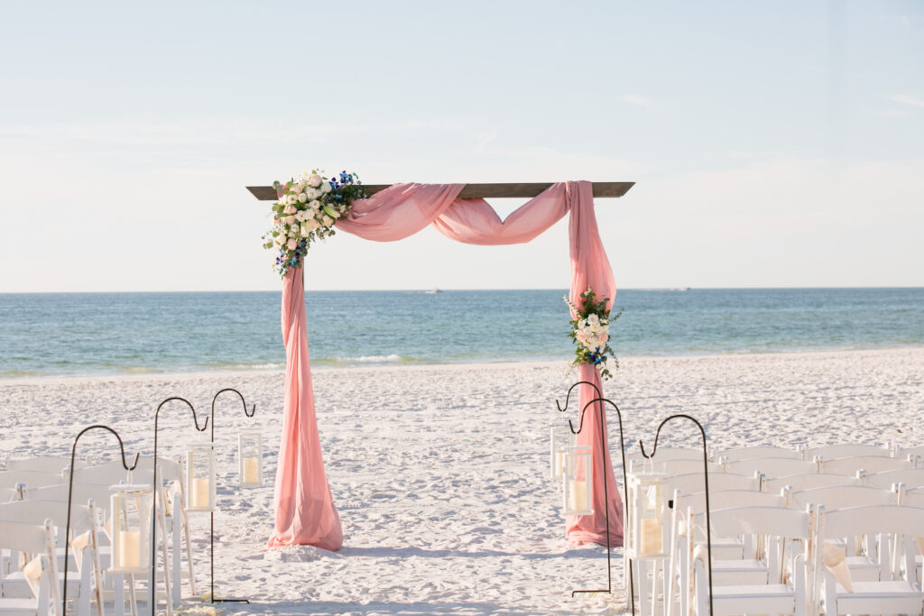 Classic Simple Wedding Beach Ceremony Decor, Hanging Candles on Stakes Lining Aisle, Wooden Arch with Pink Linen and Floral Bouquets | Tampa Bay Wedding Photographer Carrie Wildes Photography | Wedding Planner Breezin' Weddings