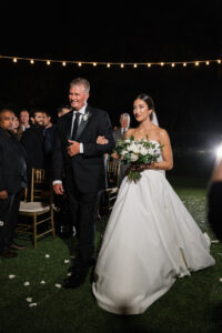 Classic Timeless Bride Walking Down the Wedding Ceremony Aisle with Father, Nighttime Wedding | Tampa Bay Wedding Hair and Makeup Femme Akoi Beauty Studio | Wedding Florist Monarch Events and Design