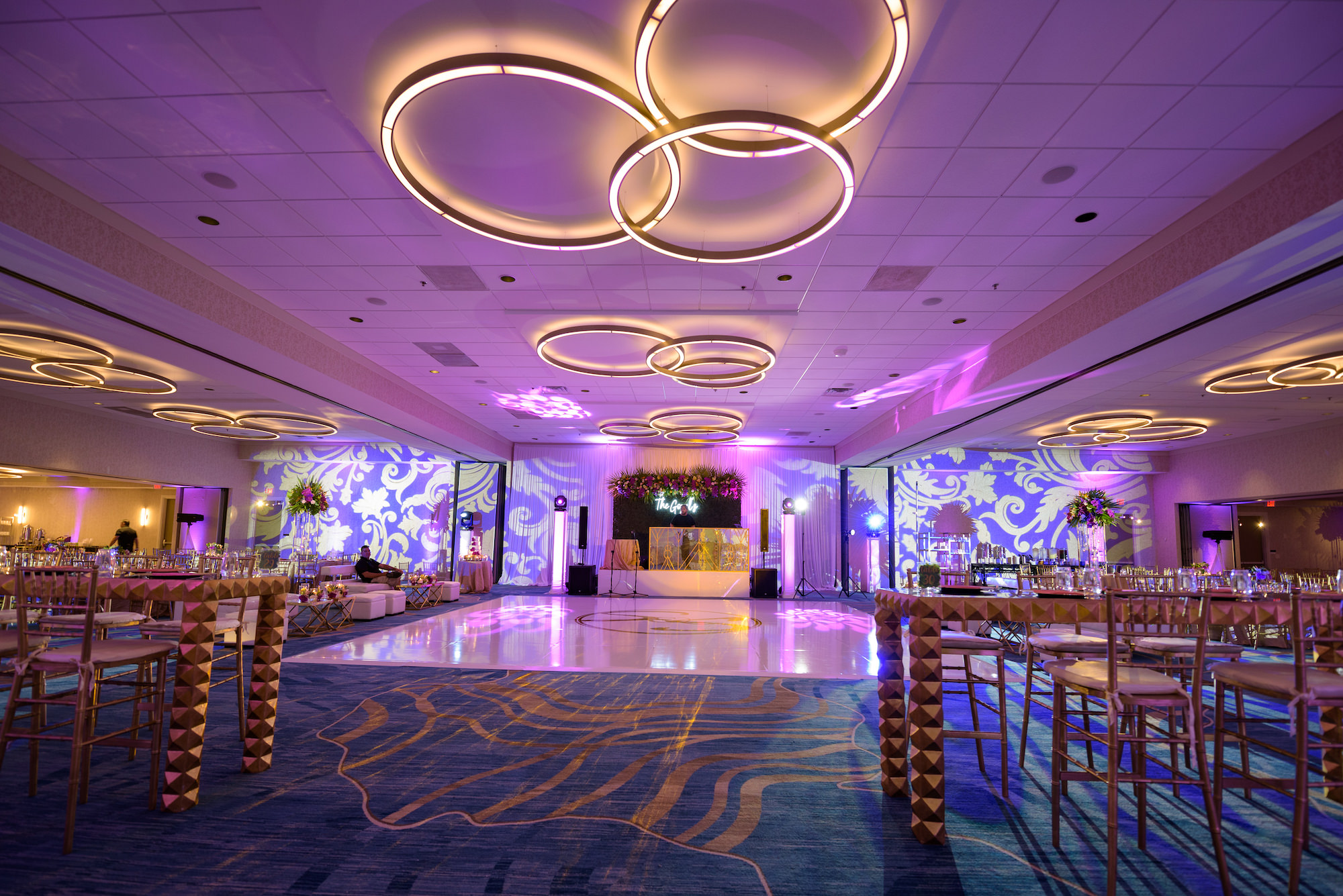 Modern Ballroom Indian Wedding Reception and Tall Centerpieces with White Monogrammed Dance Floor, Hedgewall Backdrop, Neon Sign, and Purple Uplighting | Tampa Bay Venue Hilton Clearwater Beach Resort and Spa | Gabro Event Rentals