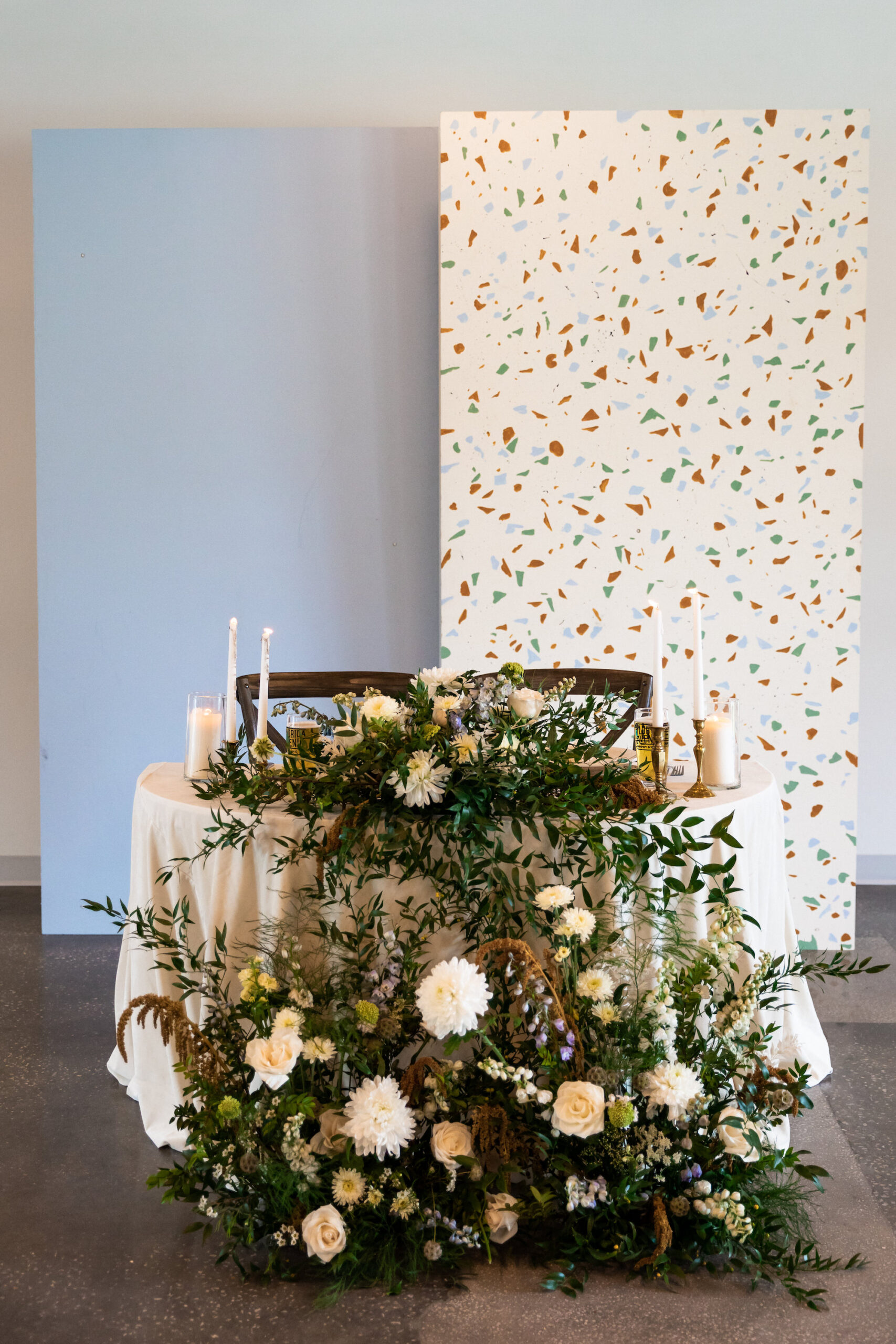 Modern Whimsical Wedding Reception Decor, Sweetheart Table with Lush Greenery and White Flowers Arrangement, Light Blue and Terrazzo Panel Backdrops