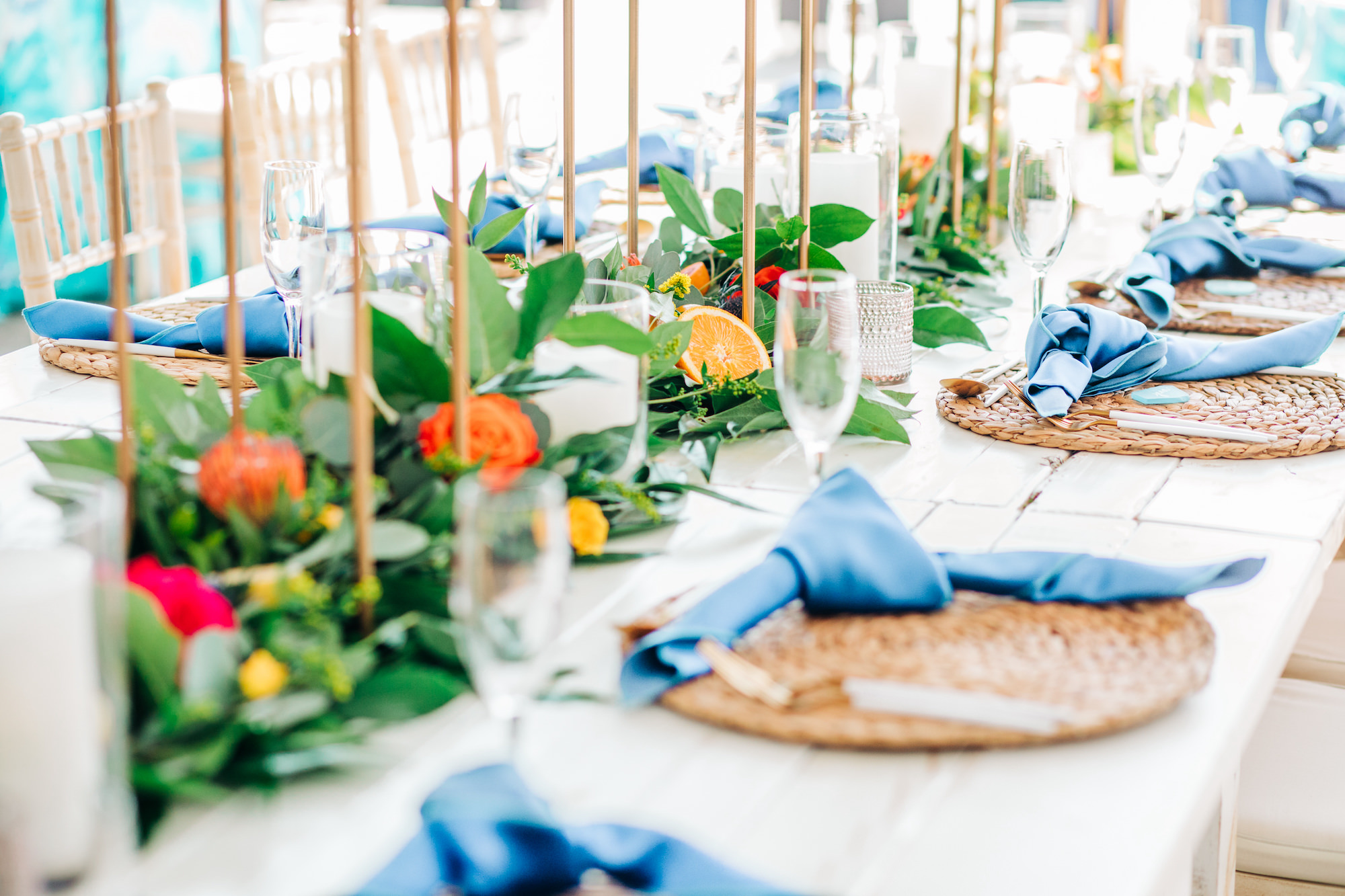 Vibrant Colorful Wedding Reception Decor, Greenery Garland with Red and Yellow Roses, Sliced Oranges,Natural Braided Grass Charger Plate, Dusty Blue Linen Napkin, White and Gold Silverware | Tampa Bay Wedding Rentals Kate Ryan Event Rentals