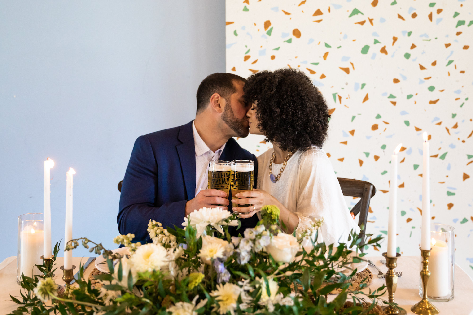 Modern Whimsical Bride and Groom with Beers, Light Blue and Terrazzo Panel Backdrops, Vintage Gold Candlesticks, Lush Greenery and White Flowers