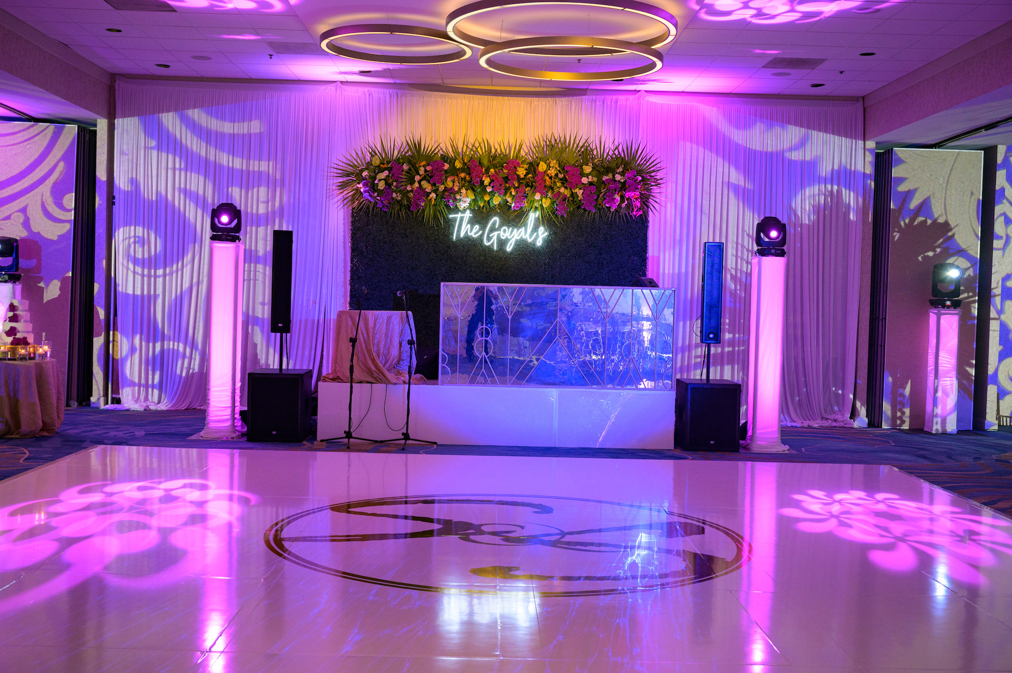 Wedding Reception and Decor, Purple Uplighting White Dance Floor with Gold Monogram, Sweetheart Table on Stage with Gold Linens, Boxwood Greenery Backdrop Wall with Custom Neon Sign, Tropical Florals with Fuchsia, Bright pink, Orange, Purple and Green | Tampa Bay Wedding Venue Hilton Clearwater Beach Resort and Spa | Gabro Event Rentals