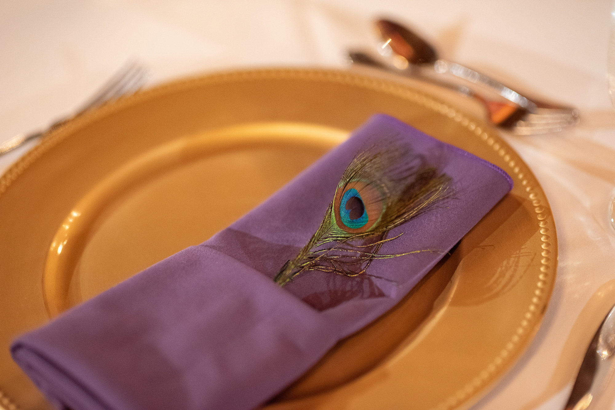 Gold Charger with Purple Napkin and Peacock Feather Detail