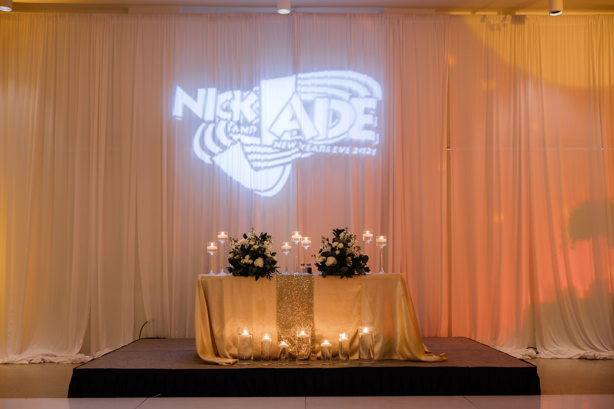 Classic Timeless New Years Eve Wedding Reception Decor, Sweetheart Table with Gold Glitter Table Linen, Floating Candles, Lush White Roses and Greenery Leaves Floral Bouquets, Space Jam Movie Inspired Personalized Projection | Tampa Bay Wedding Florist Tampa Garden Club