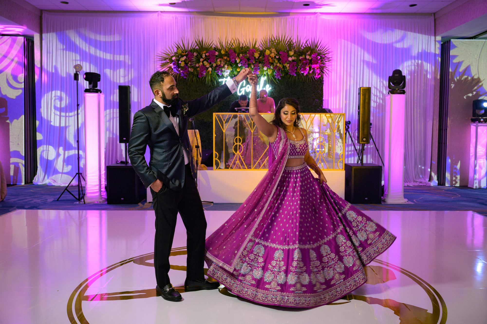 Indian Bride and Groom at First Dance on Luxurious All White Dance Floor with Gold Monogram, Bride Wearing Traditional Indian Fuchsia Lehenga and Groom Wearing Modern Black Tuxedo | Tampa Bay Hotel Venue Hilton Clearwater Beach Resort and Spa