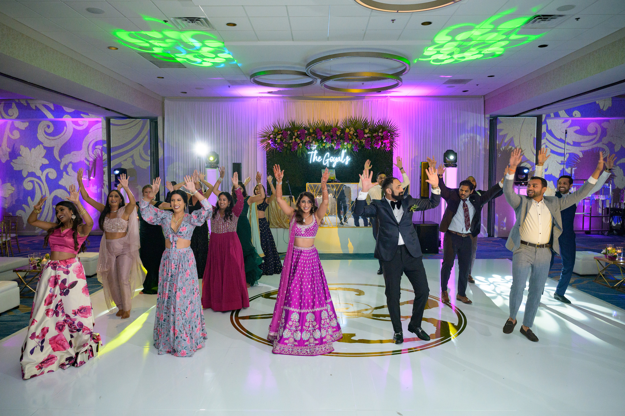 Indian Bride and Groom Dance on Luxurious All White Dance Floor with Gold Monogram, Bride Wearing Traditional Indian Fuchsia Lehenga and Groom Wearing Modern Black Tuxedo | Tampa Bay Hotel Venue Hilton Clearwater Beach Resort and Spa
