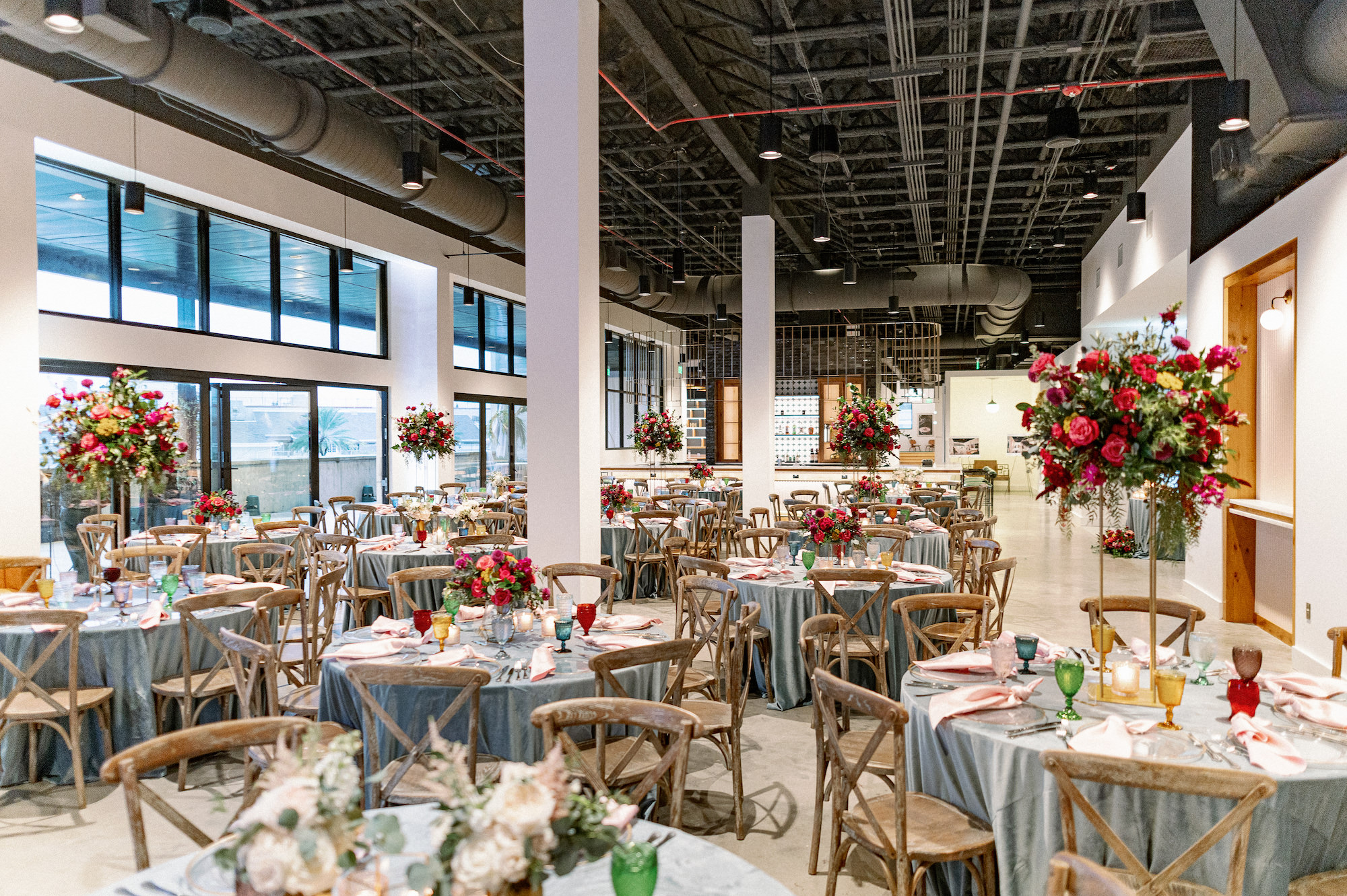 Vibrant Same Sex Lesbian Wedding Wedding Reception Decor, Round Tables with Dusty Blue Linens, Wooden Cross Back Chairs, Tall Red, Yellow and Pink Floral and Greenery Centerpieces | Tampa Bay Wedding Photographer Dewitt for Love Photography | Wedding Rentals Gabro Event Services | Industrial Modern Wedding Venue Hyde House