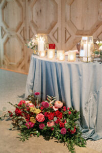 Vibrant Wedding Reception Decor, Sweetheart Table with Dusty Blue Linen, Gold Geometric Candle Holders, Lush Floral Arrangement, Greenery Leaves, Red, Pink Roses, Yellow, Fuschia FLowers | Tampa Bay Wedding Photographer Dewitt for Love Photography | Wedding Rentals Gabro Event Services