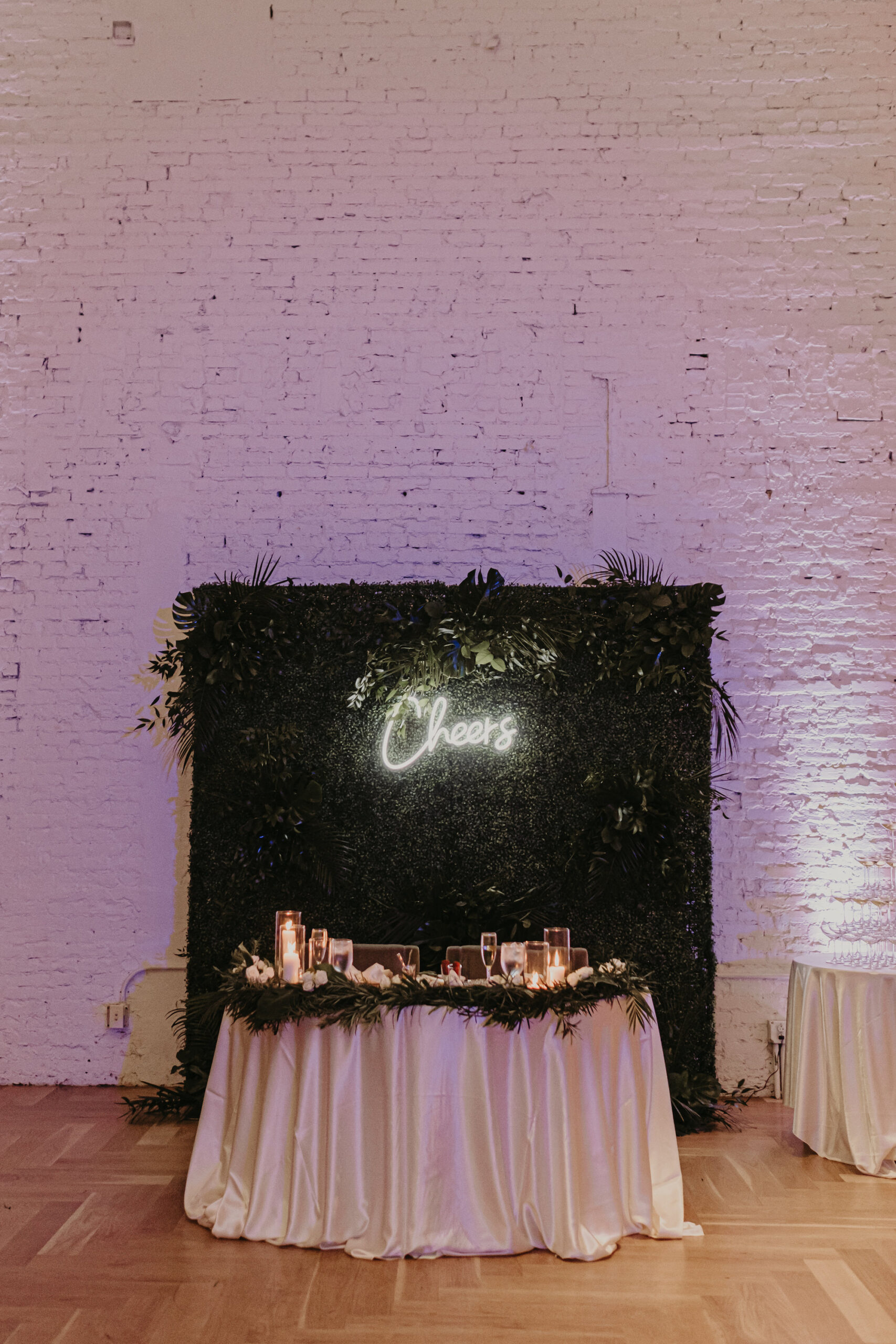 Tropical Greenery Wall Backdrop | Sweetheart Candlelit Head Wedding Reception Table Inspiration with Neon Cheers Sign