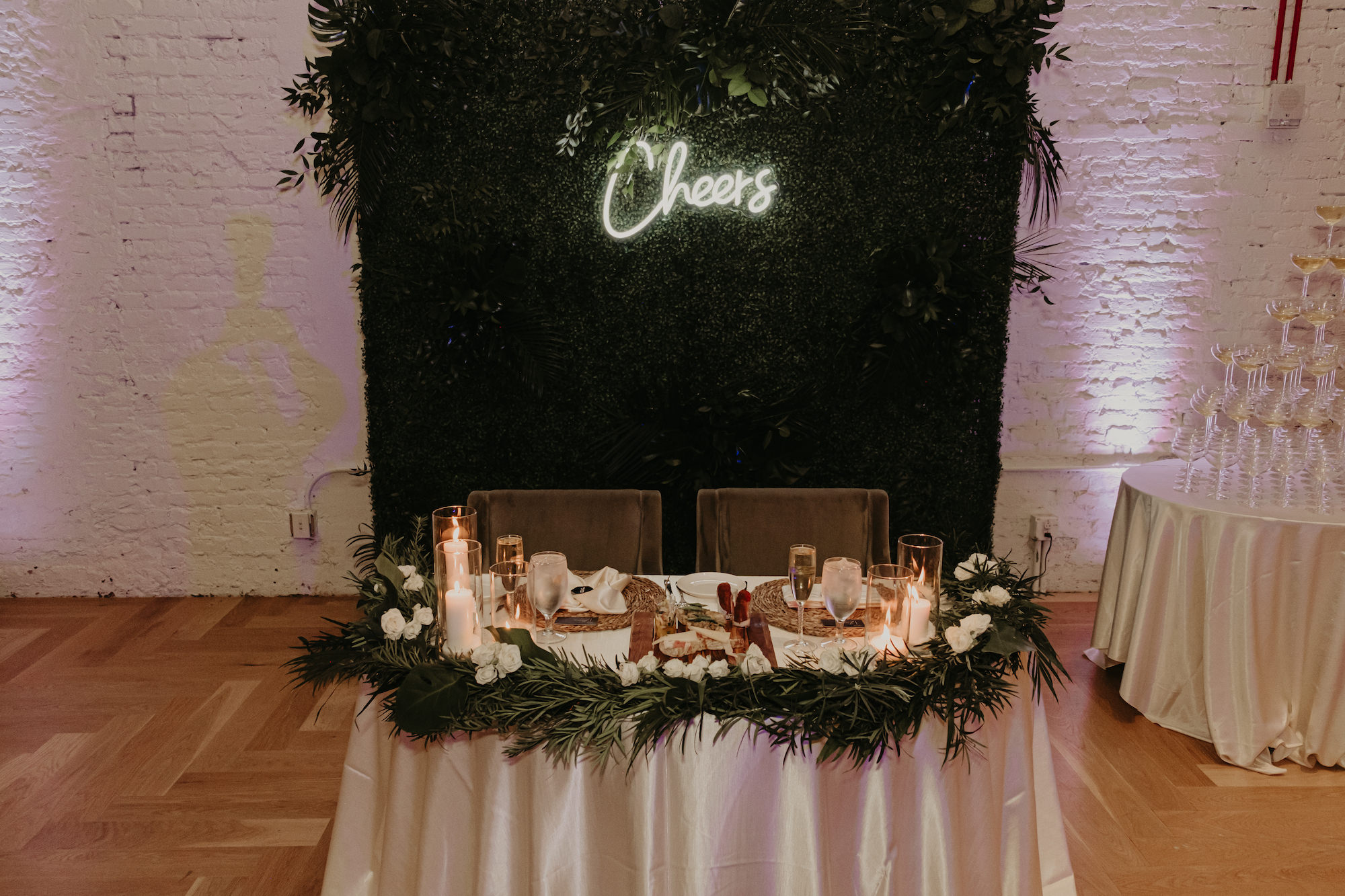 Tropical Greenery Wall Backdrop | Sweetheart Candlelit Head Wedding Reception Table Inspiration with Neon Cheers Sign