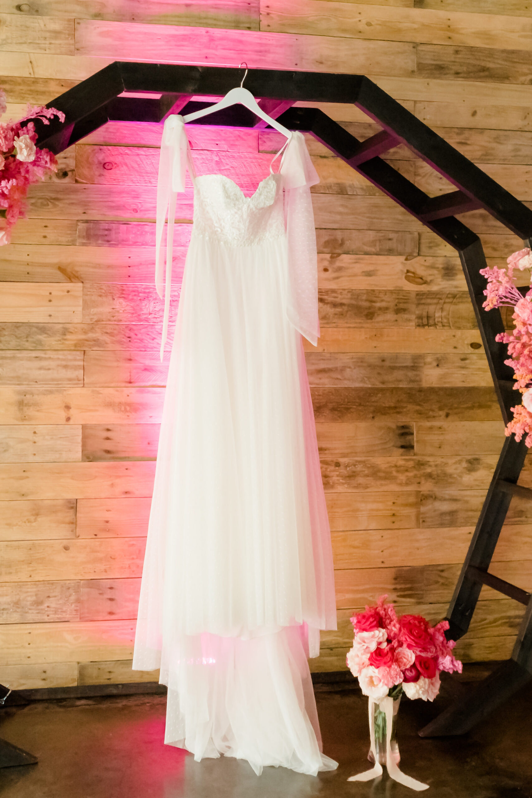 Whimsical Tulle Wedding dress Hanging on Geometric Black Arch with Pink Uplighting