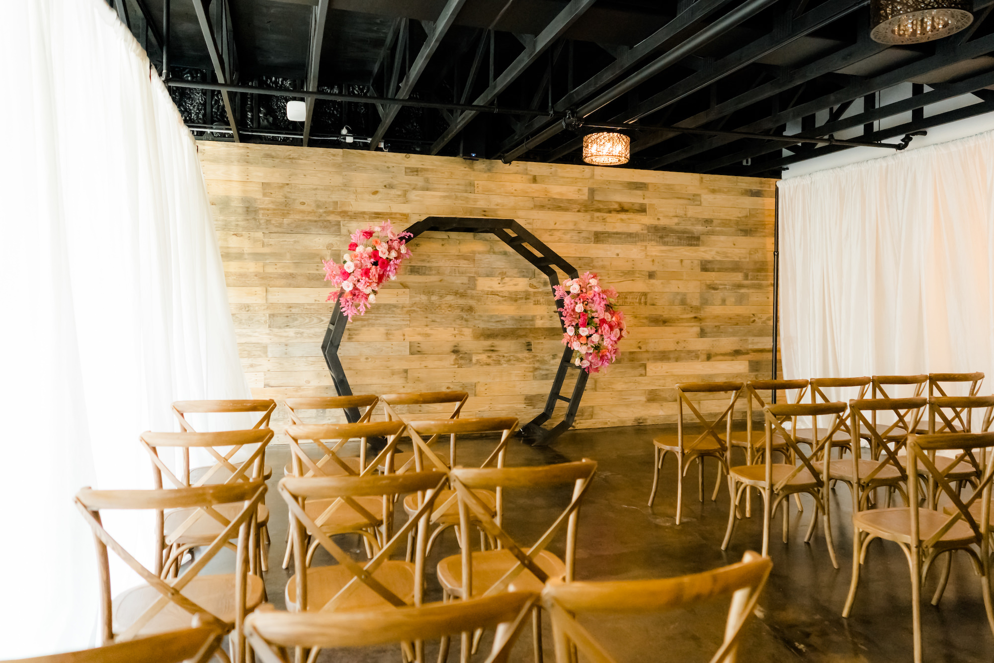 Rustic Boho Wedding Ceremony Decor, Wooden Cross Back Chairs, Black Geometric Arch with Lush Pink and Fuchsia Flower Arrangements | St. Pete Beach Wedding Venue The West Events