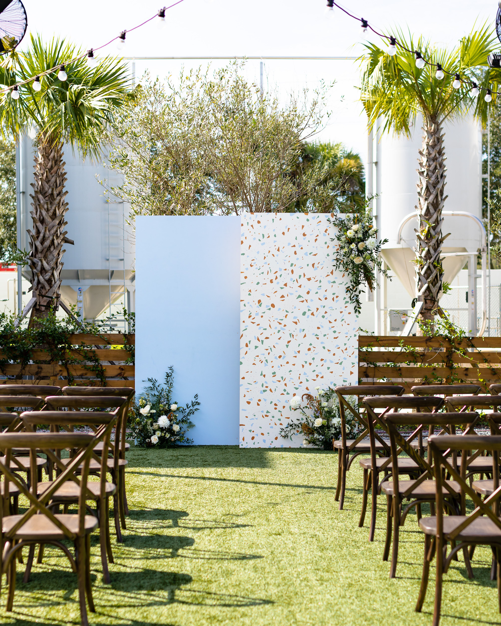 Modern Whimsical Wedding Ceremony Decor, Wooden Cross Back Chairs, Hanging Bistro Lights, Light Blue and Terrazzo Backdrop | Florida Avenue Brewing Co.