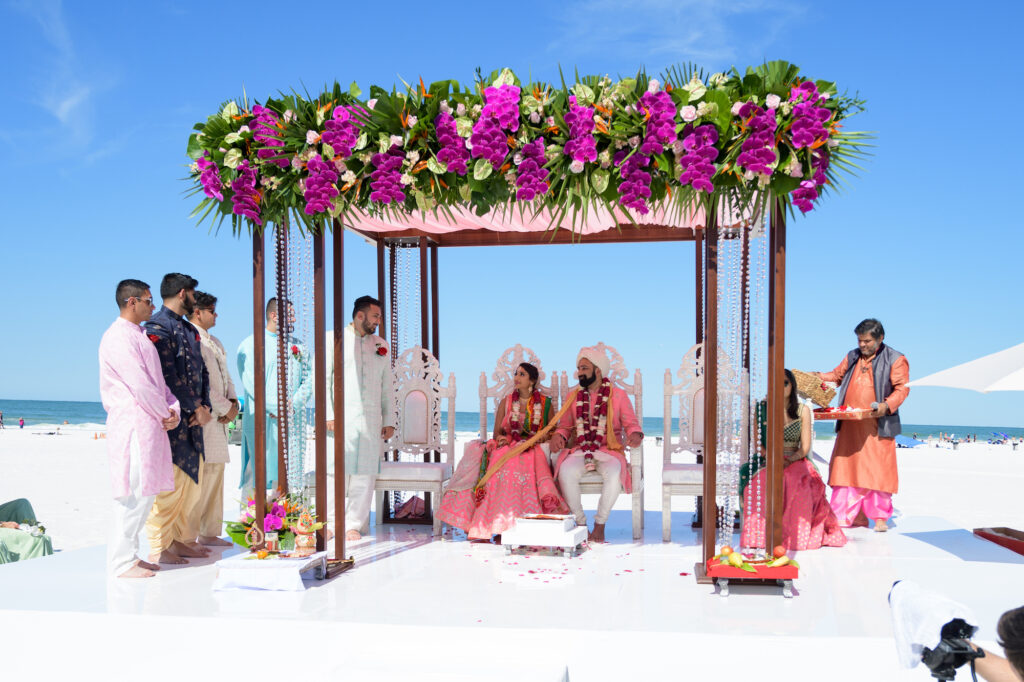 Outdoor Florida Beachfront Indian Wedding Ceremony, Bride and Groom under Hindu Mandap Altar Decorated with Tropical Flowers and Orchids in Purple, Fuchsia, Green and Orange with Palm Leafs | Tampa Bay Destination Wedding Venue Hilton Clearwater Beach