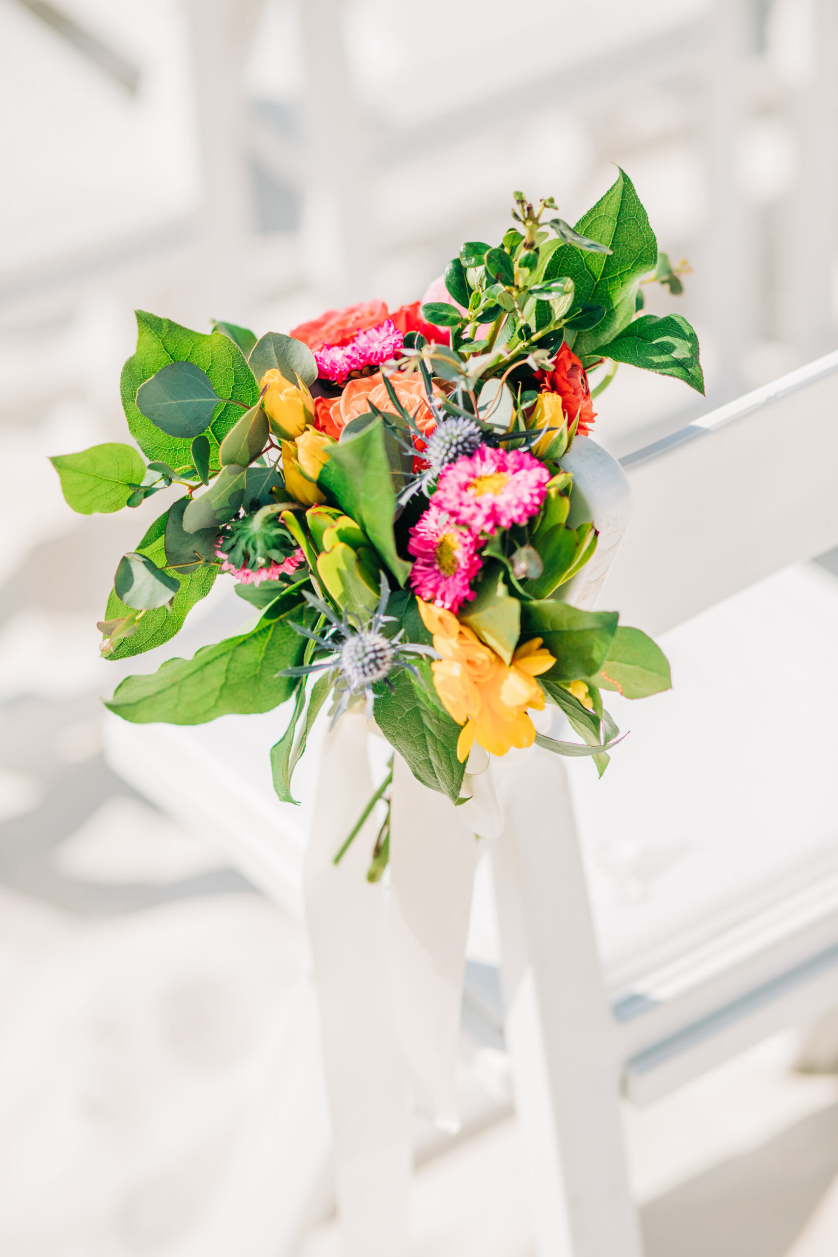 Vibrant Colorful Same Sex Wedding Ceremony Decor, Yellow and Pink Flowers with Greenery and Blue Thistle Floral Arrangement on Chair