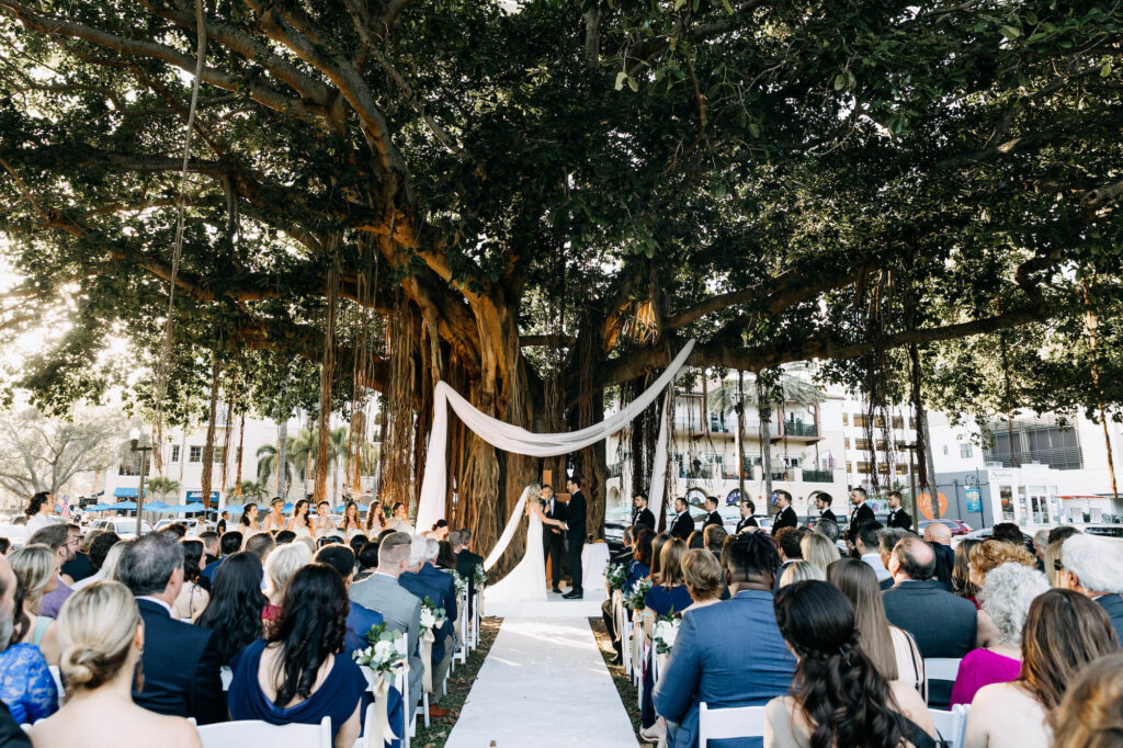 Nature Inspired Banyan Tree Outdoor Wedding Ceremony Altar Ideas | White Drapery with Wooden Cross | Tampa Bay Wedding Planner Wilder Mind Events | Tampa Bay Videographer J&S Media | Downtown St. Pete Venue N. Straub Park