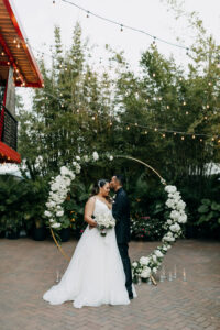Bride and Groom Wedding Portrait, Simple Classic Outdoor Bamboo Courtyard Wedding Decor, Hanging Bistro Lights, Round Circular Gold Metal Arch with Lush White and Greenery Flowers | Tampa Bay Wedding Photographer Amber McWhorter Photography | St. Pete Wedding Florist Save the Date Florist | Wedding Venue NOVA 535