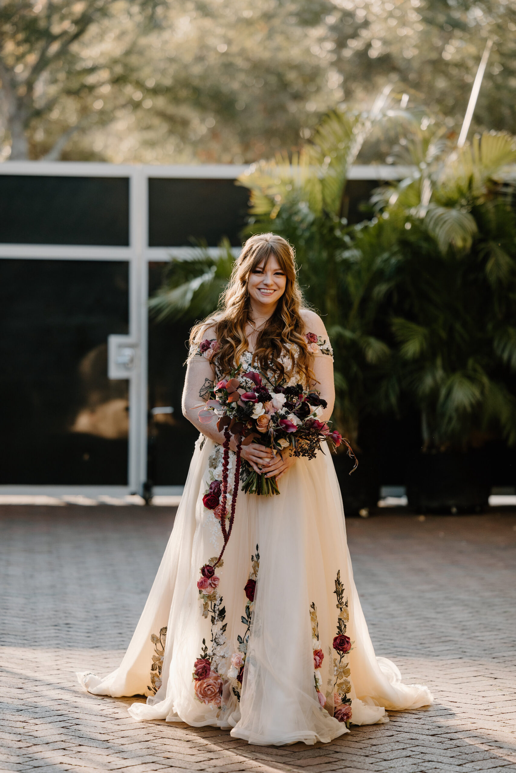 Bride Walking Down the Wedding Ceremony Aisle | Dark Moody Floral Bridal Wedding Bouquet | Off the Shoulder Nude and Red, White, Green, and Blush Pink Floral Applique A-Line Wedding Dress with Chapel Length Train