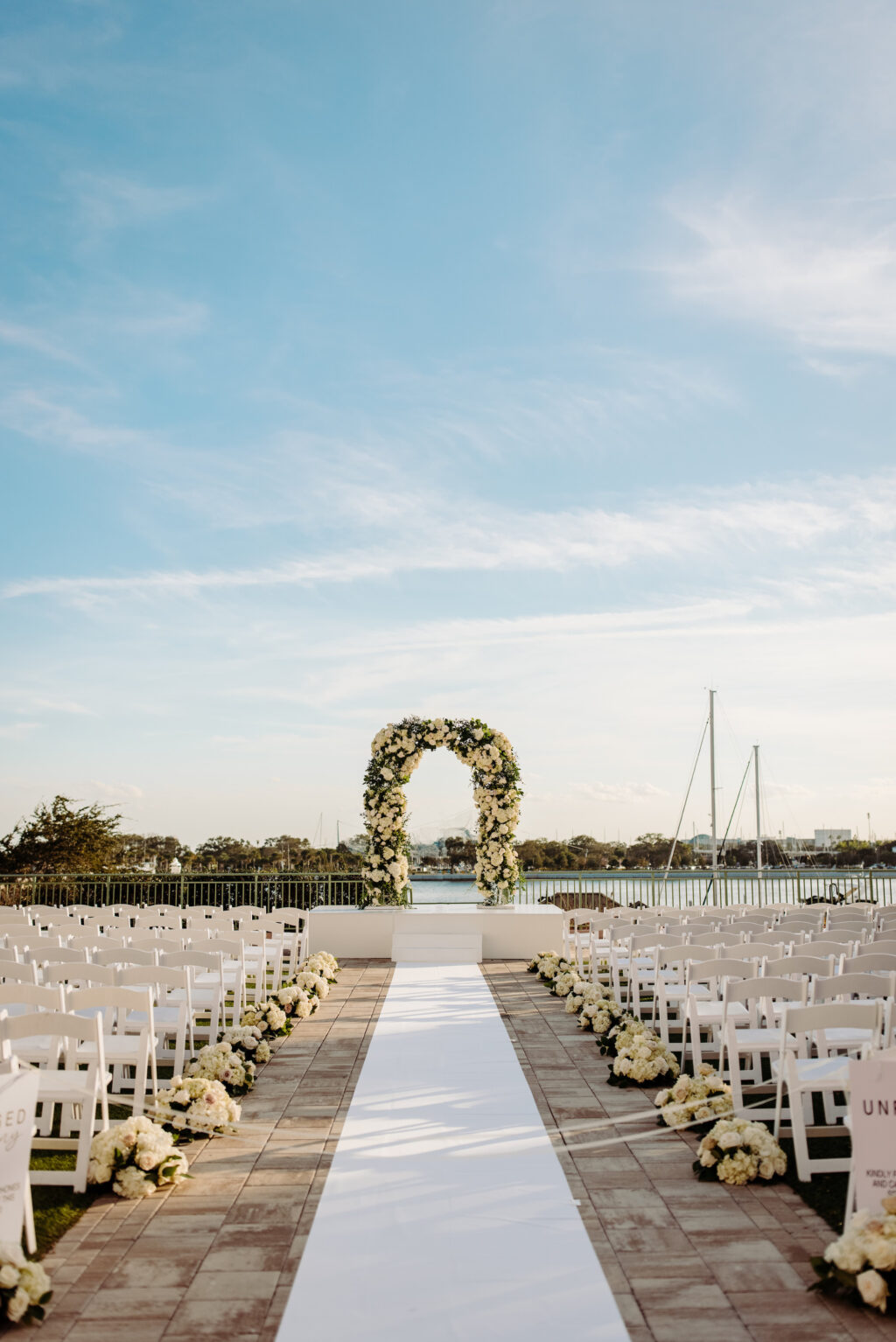 Luxurious White Rose, Hydrangeas, and Greenery Wedding Ceremony Arch with White Stage Ideas | White Aisle Runner Floral Aisle Decor Inspiration | Downtown St. Pete Venue Renaissance Vinoy