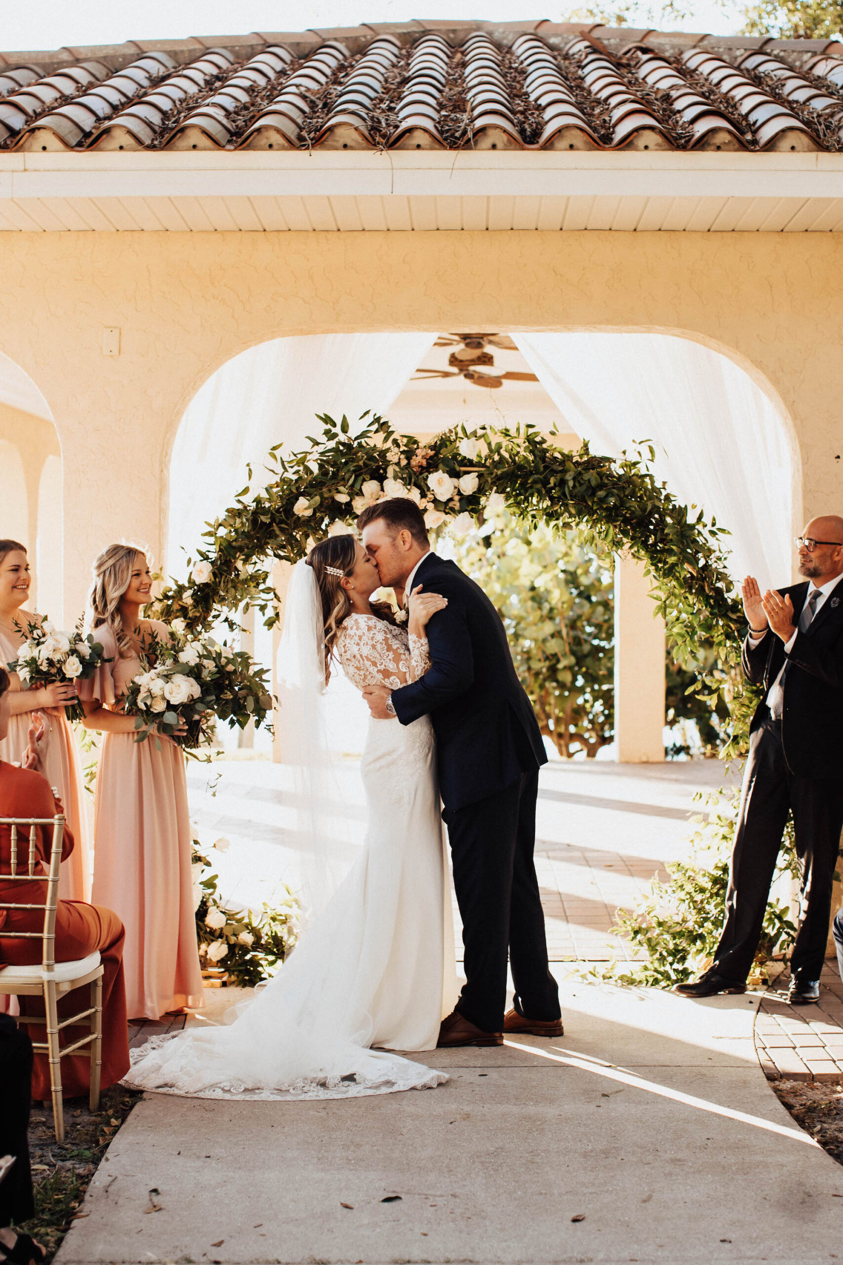 Bride and Groom First Kiss in Outdoor Wedding Ceremony with Greenery Arch