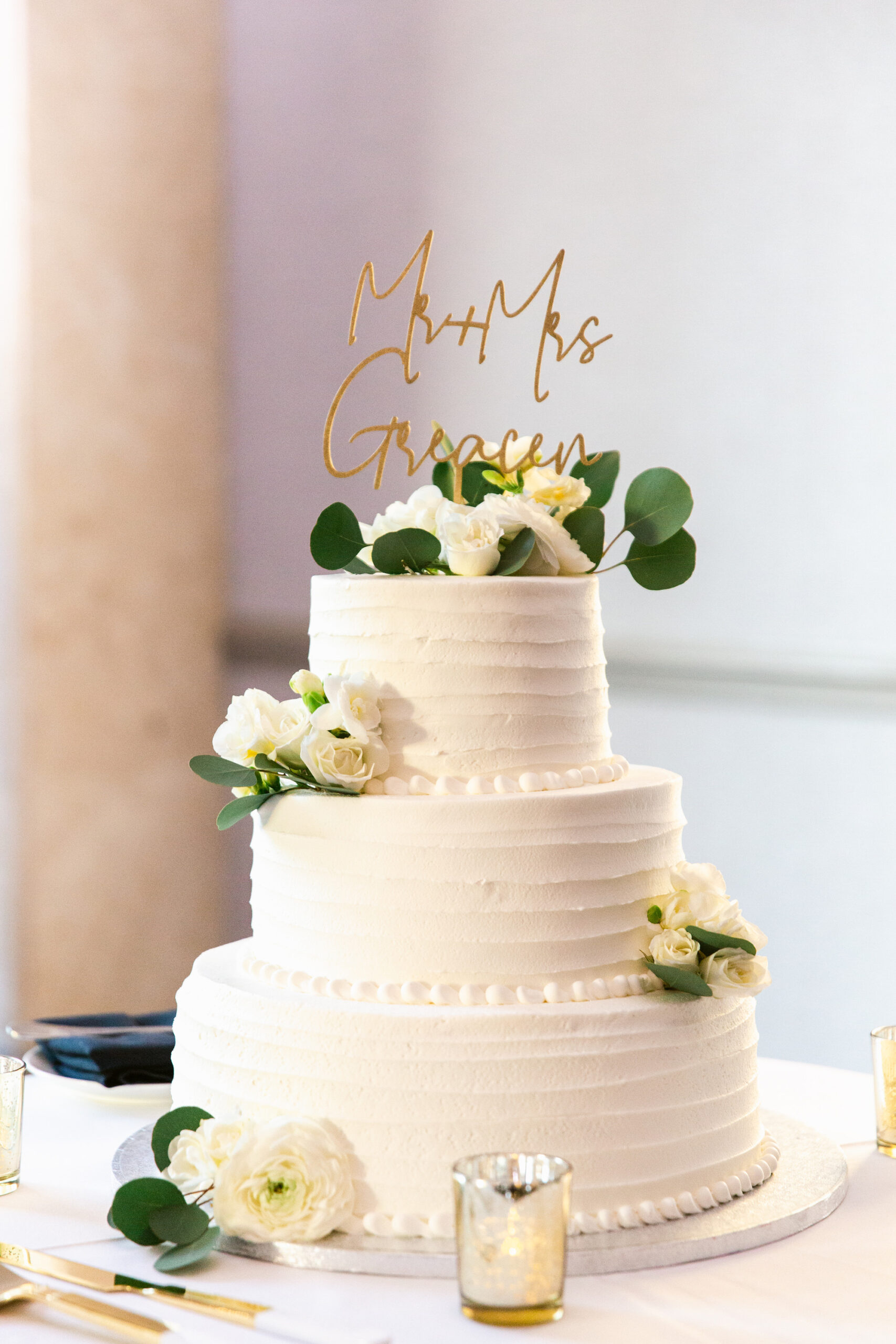 Classic White Three Tier Round Wedding Cake Decorated with White Roses and Green Eucalyptus Leafs, Modern Gold Script Mr. and Mrs. Last Name Wedding Topper