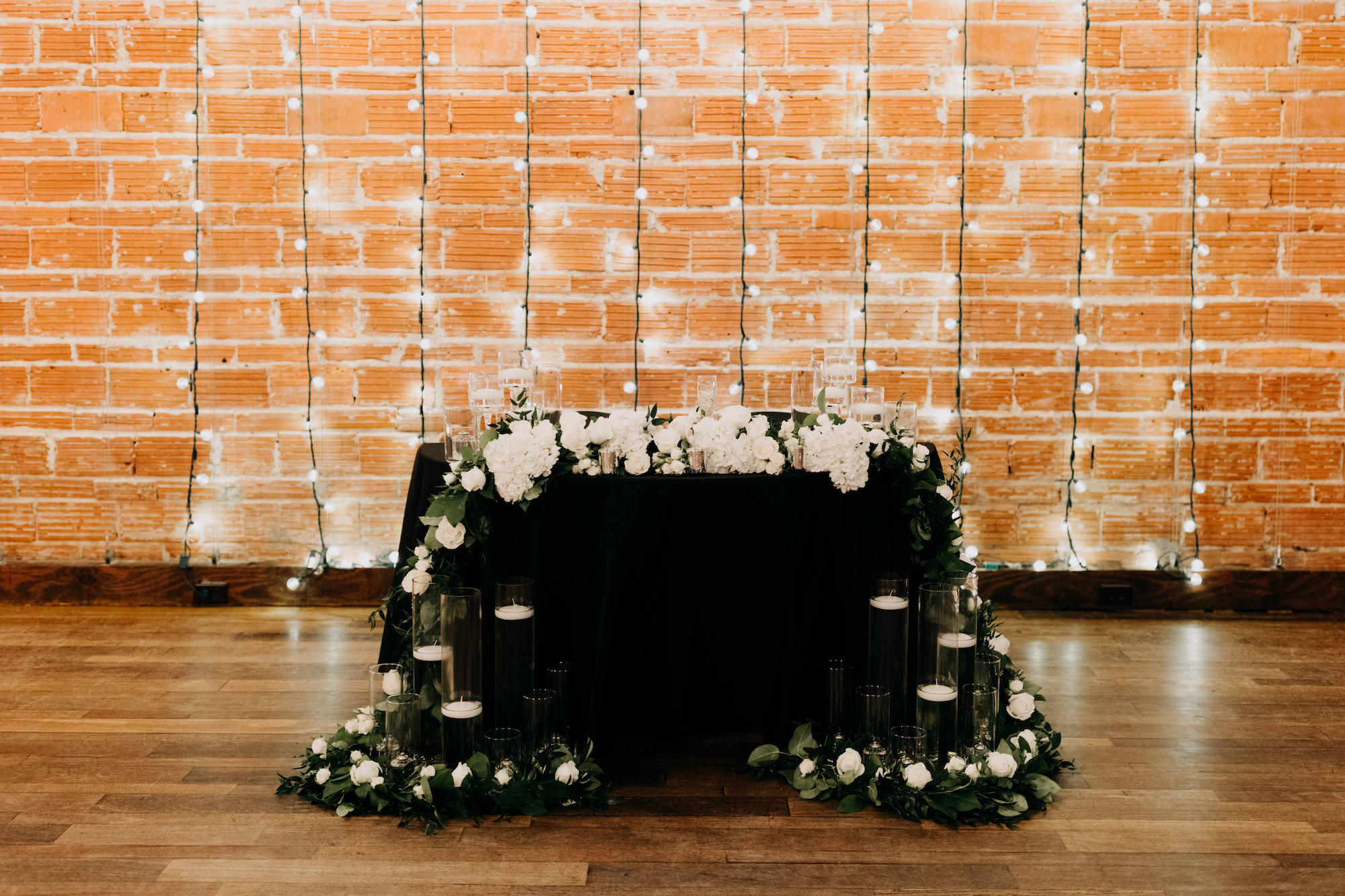 Simple Classic Black and White Wedding Reception Decor, Sweetheart Table with Floating Candles, White Hydrangeas Flowers, Red Brick Wall Backdrop and Hanging Lights | Tampa Bay Wedding Photographer Amber McWhorter Photography | Unique Industrial Wedding Venue NOVA 535 | Wedding Florist Save the Date Florist