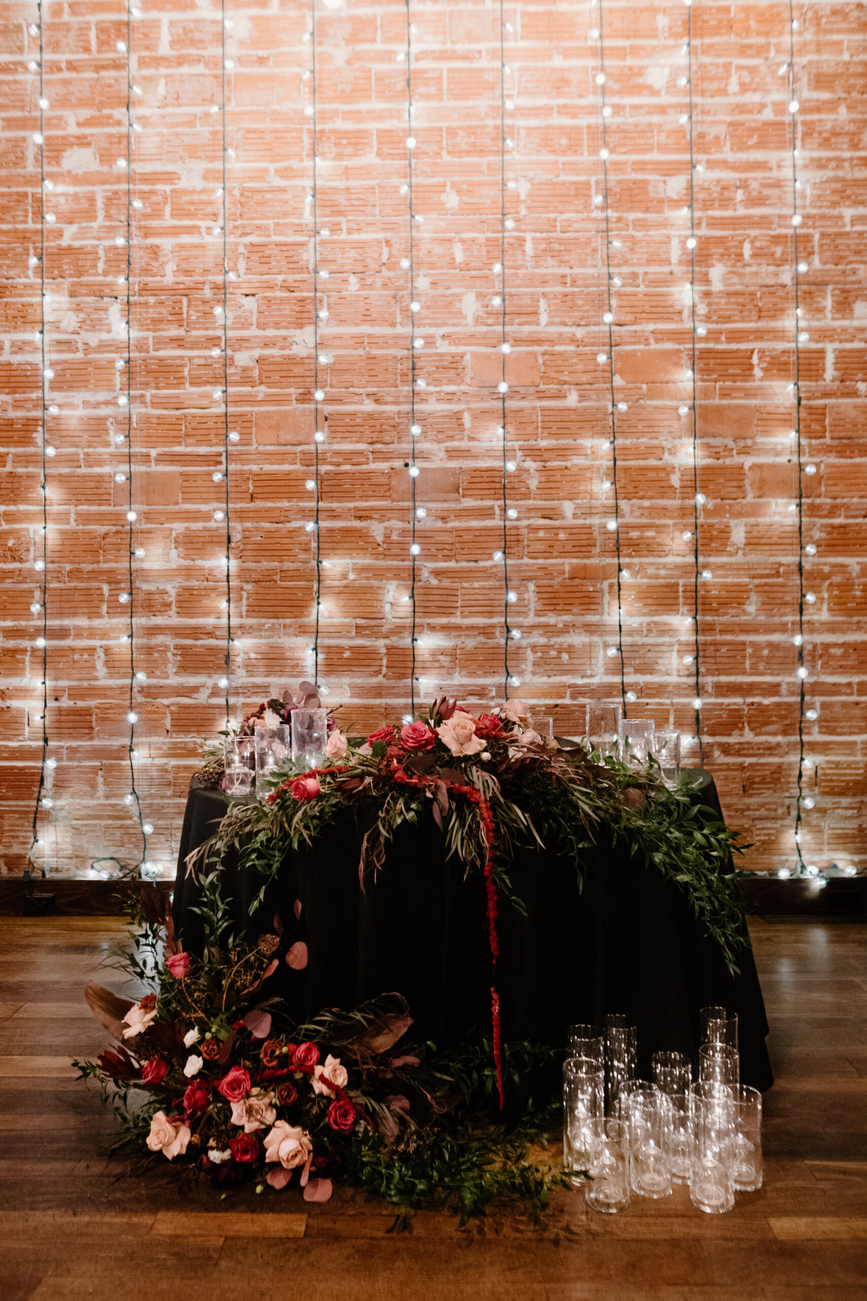 Dark and Moody Sweetheart Head Table with Edgy Floral Arrangements | Hanging Market Lights Backdrop | Romantic Goth Wedding Inspiration