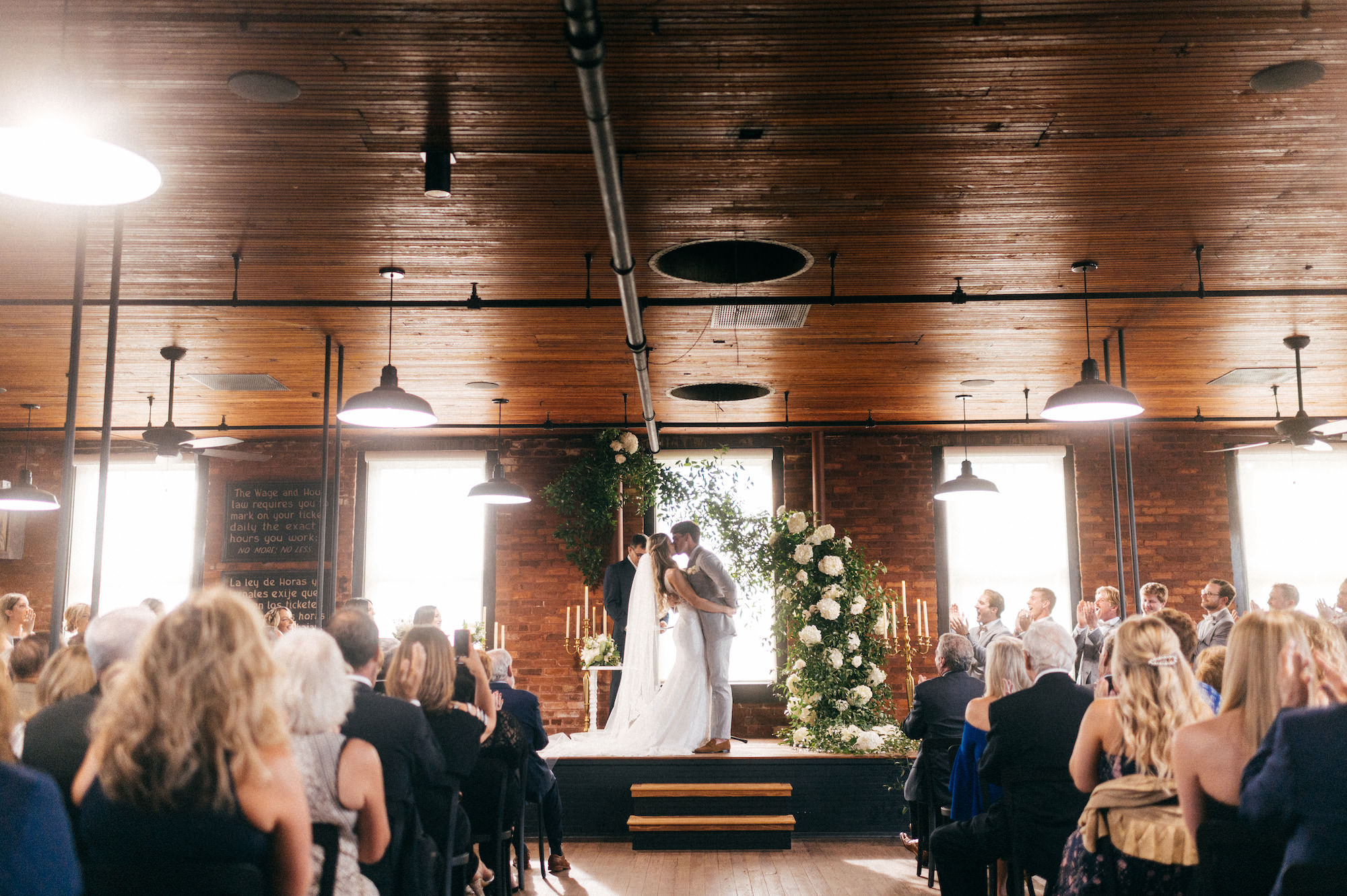 Bride and Groom Wedding Vows Kiss. Greenery Ceremony Arch with White Flowers| Tampa Bay Wedding Venue J.C. Newman Cigar Co. | Florida Wedding Planner Parties A La Carte | Florist Bruce Wayne Florals