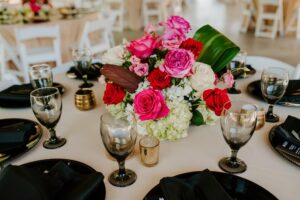 Modern Tropical Wedding Reception Decor Inspiration | Black Chargers, Napkins, and Glassware with Pink Fuchsia Rose and Hydrangea Centerpieces and Champagne Linens | Tampa Bay Rentals Gabro Event Services