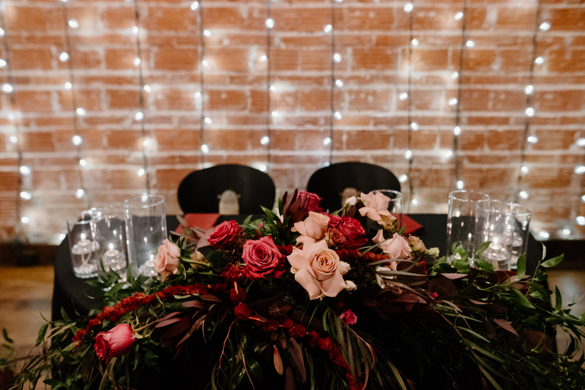 Dark and Moody Sweetheart Head Table with Edgy Floral Arrangements | Hanging Market Lights Backdrop | Romantic Goth Wedding Inspiration