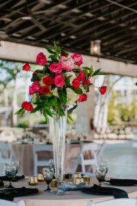 Modern Tropical Wedding Reception Decor Inspiration | Black Chargers, Napkins, and Glassware with Tall Pink Fuchsia Rose and Hydrangea Centerpieces in Glass Vase and Champagne Linens